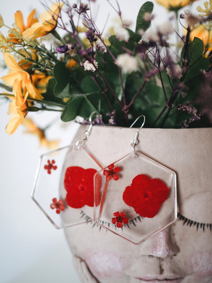 Close-up of handmade resin earrings with red flowers in a decorative flowerpot for an artistic touch.